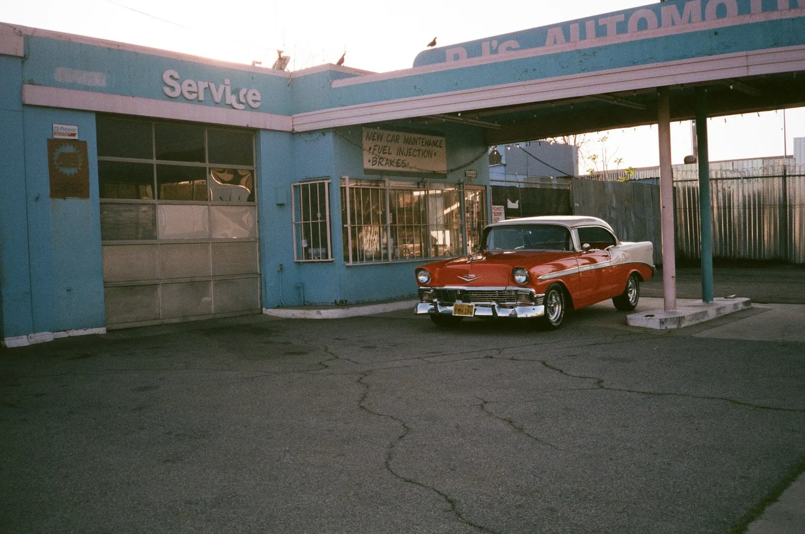 Red and white vintage car parked beside blue and white building during daytime