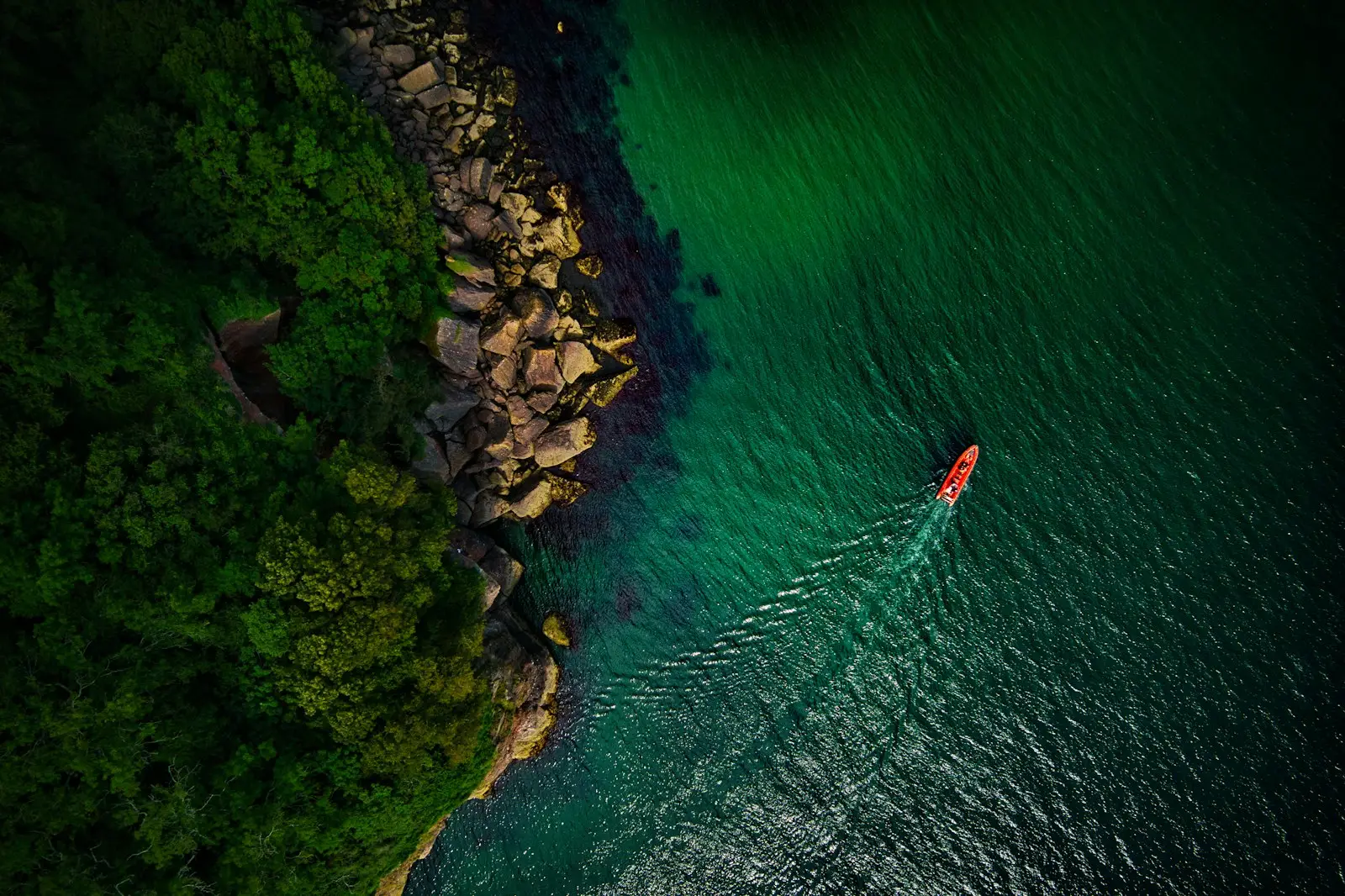 Red Rocks - A red powerboat hugs the shore on a beautiful Summer morning in Devon, UK