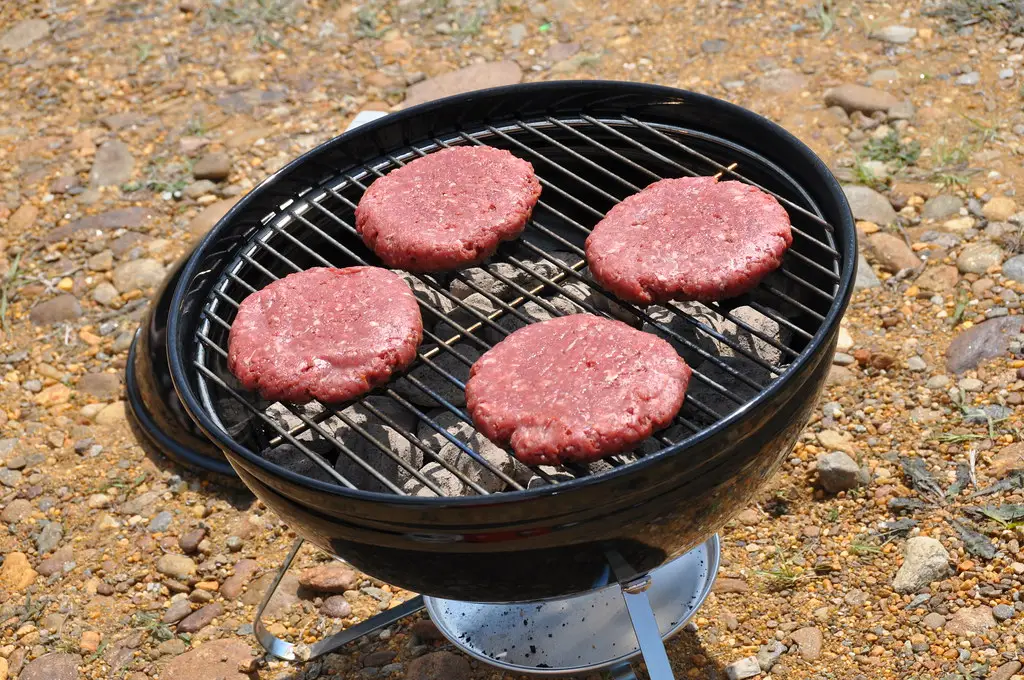 Burgers on a portable charcoal grill in a gravel tailgate parking lot