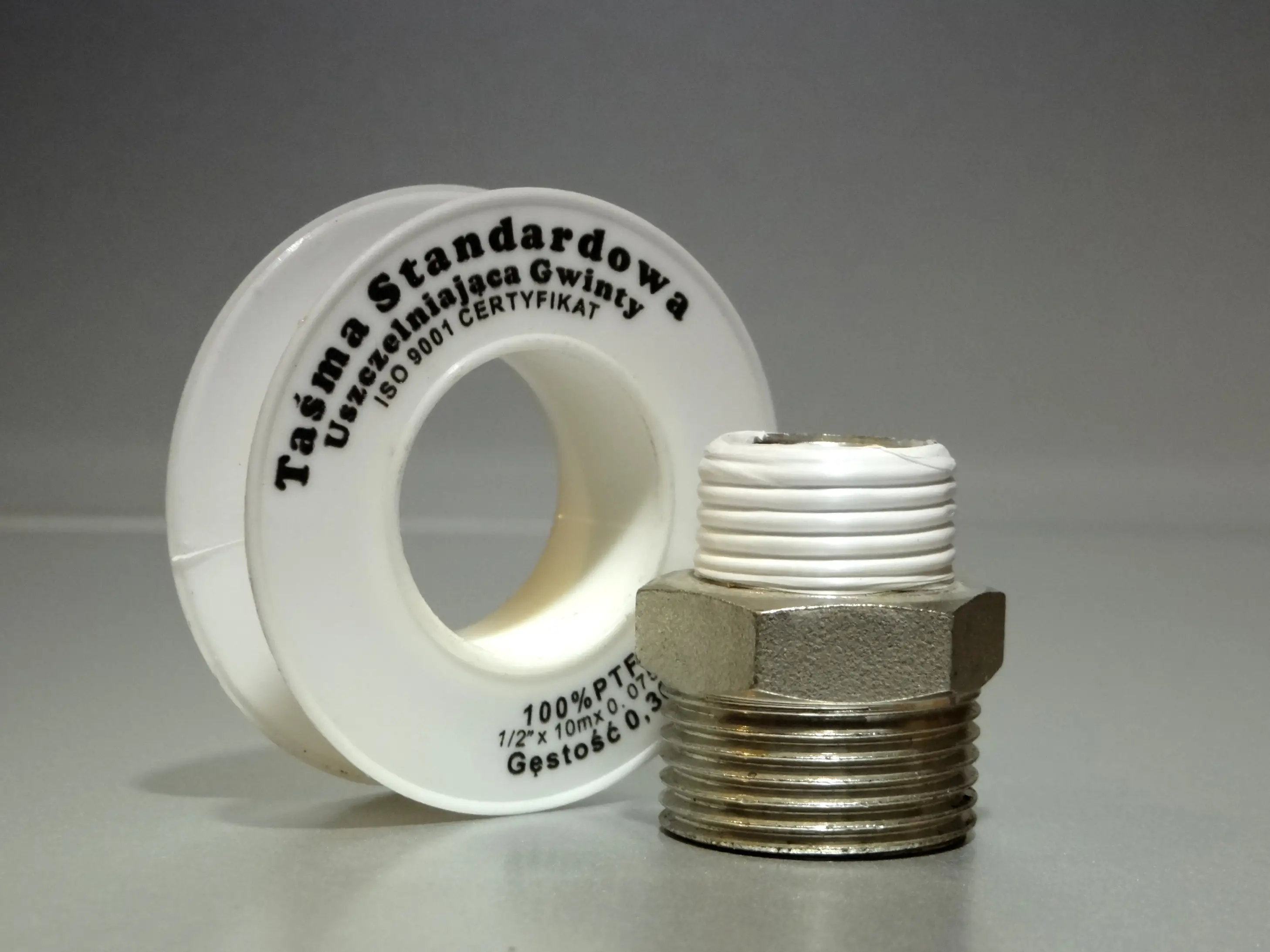 Roll of white PTFE thread seal tape next to a brass pipe fitting with taped NPT threads